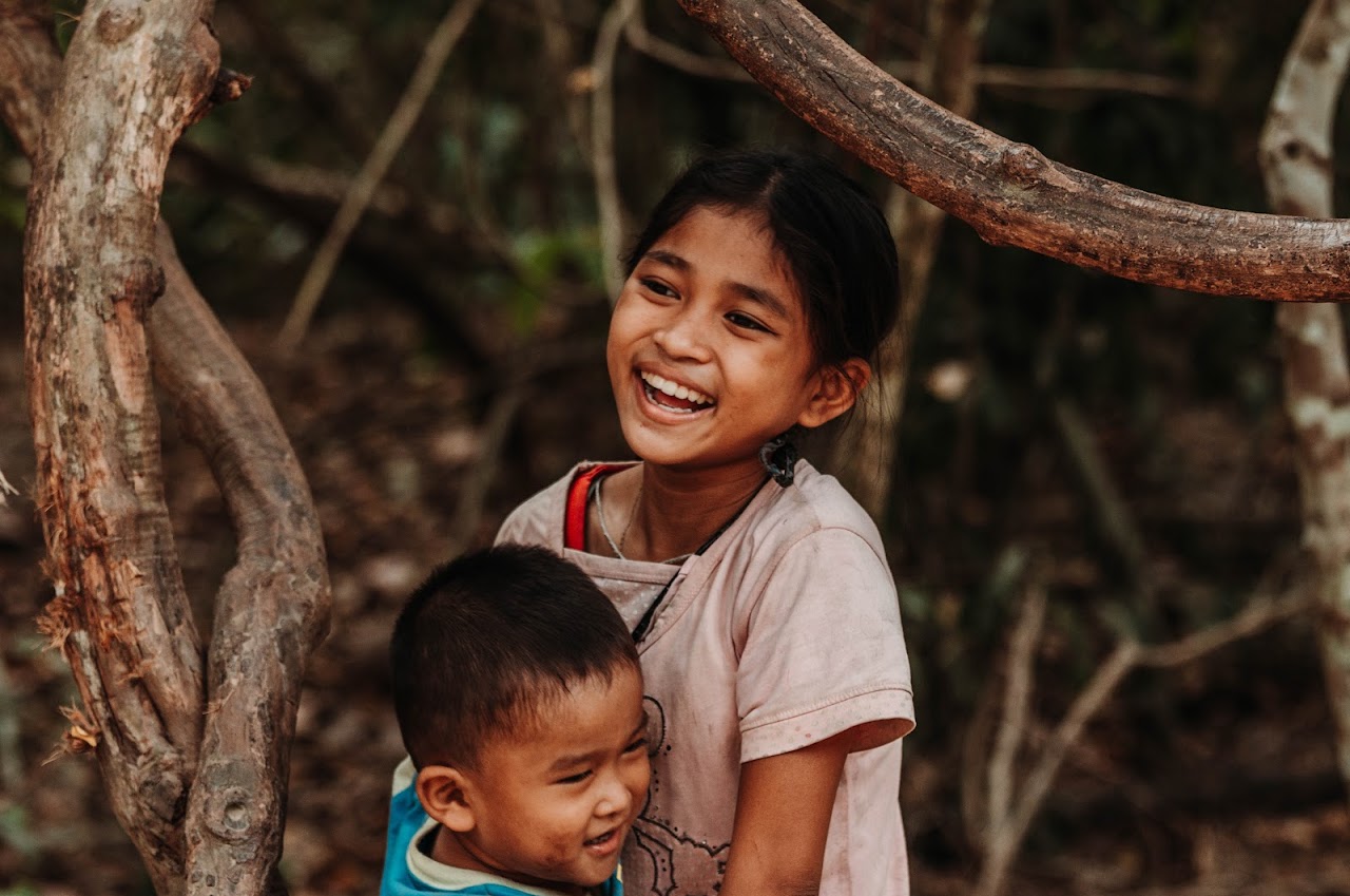 Two children are joyfully playing outdoors in a wooded area.