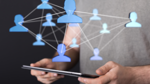 A person holding a tablet with a digital network of blue human icons connected by lines.